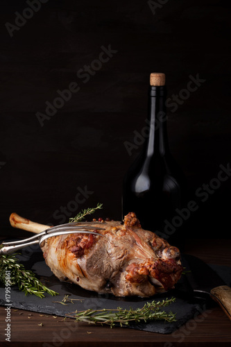 swiezo-pieczona-jagnieca-noga-z-ziolami-i-butelka-czerwonego-wina-na-ciemnym-tle