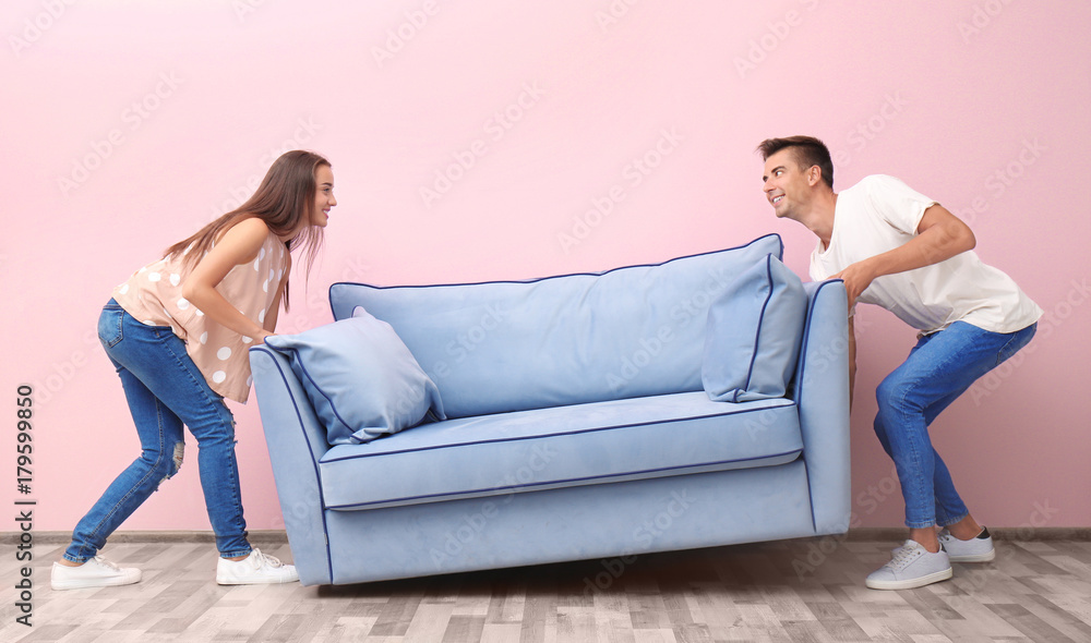 Young couple carrying blue sofa near color wall