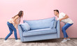 © Africa Studio - Young couple carrying blue sofa near color wall