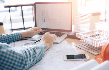 Architect sitting in modern office using computer working project and looking blueprint on screen.