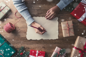 Wall Mural - A woman writing on craft paper in the center of christmas gifts on a wooden table