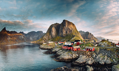 Norwegian fishing village at the Lofoten Islands in Norway. Dramatic sunset clouds moving over steep mountain peaks