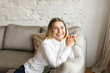 © shurkin_son - Joyful positive mature female dressed in white blouse relaxing in her living room. Beautiful elegant middle aged woman feeling happy and relaxed while having rest on comfortable sofa at home