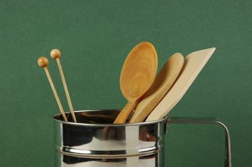 Wall Mural - wooden kitchenware in metal jug  on old wooden table over green background