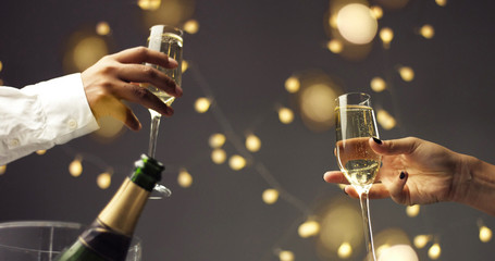 Wall Mural - Close up of dark skinned man and caucasian woman toasting with glasses of sparkling wine on gray background with lights and lens flare