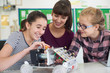 © highwaystarz - Teacher Talking To Female Pupils Studying Robotics In Science Lesson