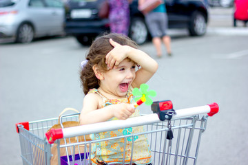 Sticker - Little kid girl sitting in a shopping cart near mall.