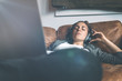 © Alex from the Rock - Attractive young happy woman listening to music in headphones with pleasure at coworking office, lying on sofa, using laptop, enjoying and resting.