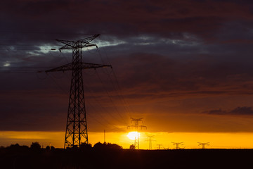 Wall Mural - High voltage power lines and transmission towers at sunset. Poles and overhead power lines silhouettes in the dusk. Electricity generation and distribution. Electric power industry and nature concept