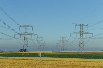 Wall Mural - High voltage power lines and transmission towers in agricultural fields in Normandy, France. Electricity generation and distribution. Electric power industry, nature and agriculture concept