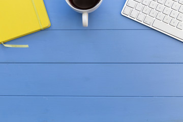 Wall Mural - Computer keyboard, coffee cup and notebook on blue wood desk