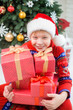© Andrii Oleksiienko - Closeup portait of smiling funny little kid holding many red presents decorated with golden ribbons. Small boy celebrating Christmas with family. Vertical color image.
