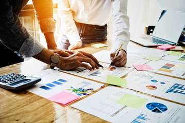 Young businessmen and partnership holding a pen pointing the graph to analyze the marketing plan with calculater and laptop computer on wood desk in office.