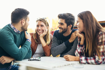 Wall Mural - Group of four friends having fun a coffee together. Two women and two men at cafe talking laughing and enjoying their time