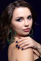 Wall Mural - Portrait of beautiful brunette woman on black background and peacock feather earrings