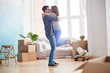 © Seventyfour - Profile view of loving young couple expressing their feeling while standing at living room of new apartment, interior design items and moving boxes on background