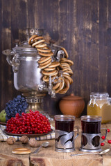 Russian traditional kettle samovar on the wooden table. Black tea, bagels, red viburnum, jam and russian samovar in the rustic style.