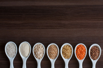 An even row of cereals in the same white dishes on a dark wooden background