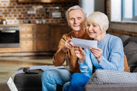happy couple. positive nice aged couple sitting on the sofa and looking at the piece of paper while 