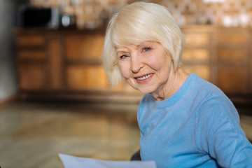 Wall Mural - Happy smile. Portrait of a nice delighted retired woman sitting at home and smiling while being in a positive mood