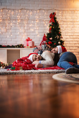 Wall Mural - Romanic lovely couple with Santa hats and blanket sleeping on a carpet together at warm home for Christmas holidays.