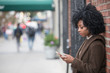 © Haydiddle - Woman using a mobile phone while standing against wall