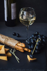 Wall Mural - Cheese plate served with crackers, grapes and glass of white wine on dark background.