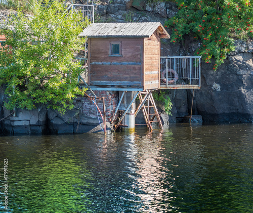 House By The Water On Stilts Against The Background Of Rocks And