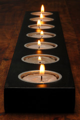 Candle holder with light as closeup on a wood table on black background    