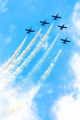 Wall Mural - Group of fighter planes fly up with a smoke track against a blue sky with clouds.