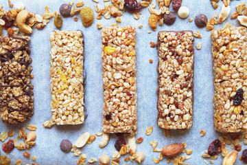 Wall Mural - Healthy granola bars with nuts, seeds and dried fruits on white baking paper. Top view.