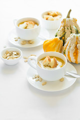 Two cups with fresh pumpkin cream soup decorated cream, seeds and crackers on white table cloth