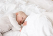© Rithor - Baby sleeping with open arms and whithout pacifier in a cradle. White pajama and white bed sheets.
