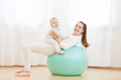 © Rithor - Happy young mother with baby wearing white sport clothes doing gymnastics with Exercise ball and having fun at light domestic home interior.