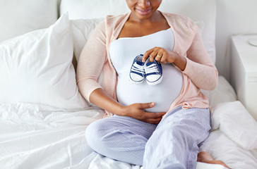 Poster - pregnant african woman with baby bootees in bed