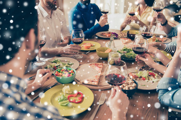 Close up of friends toasting at the party. Youth is celebrating with tasty dishes and drinks, enjoying themselves and winter vacation, snowfall xmas background