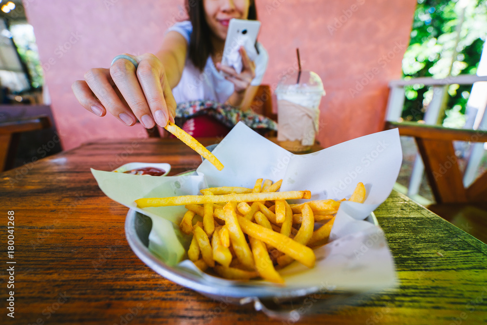 Woman eating french fries while using smart phone.