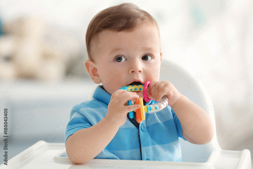 Cute baby with rattle sitting on chair indoors