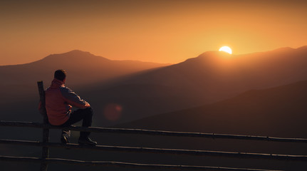 Silhouette of man who sitting on a wooden fence