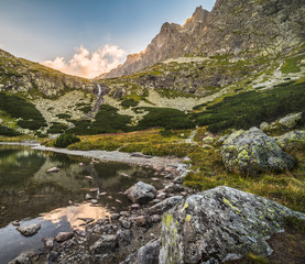 Wall Mural - Mountain Lake with Waterfall and Rocks in Foreground at Sunset. Velicka Valley, High Tatra, Slovakia.