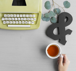 Wall Mural - A hand holding a cup of tea featuring a retro typewriter
