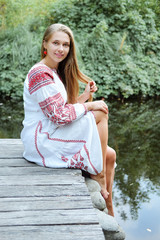 Wall Mural - Beautiful slavonic girl with long blond hair and blue eyes sitting near river