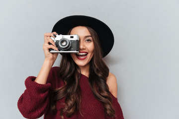 Canvas Print - Close-up portrait of young hipster brunette woman looking through the viewfinder of retro photocamera