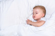 Cute one year old baby boy sleeping in a white bed
