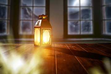 Table with space for your product or advertising tex. Candle lamp giving warm light. Window overlooking the winter mountains and the moon in the sky.