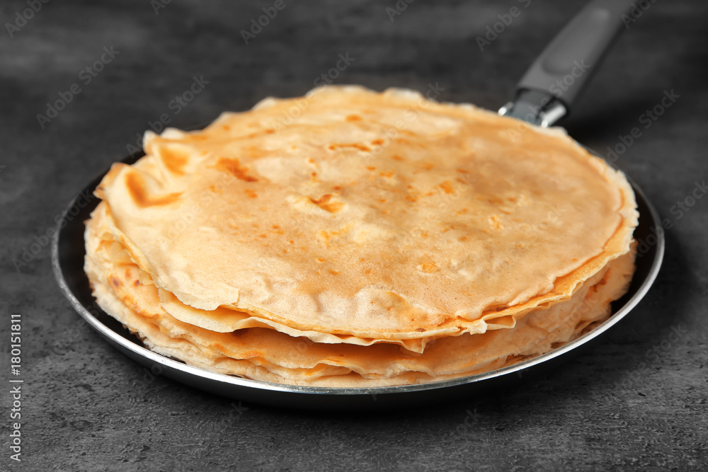 Frying pan with tasty buckwheat thin pancakes on table