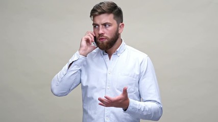 Poster - Worried bearded man in shirt talking by smartphone over gray background