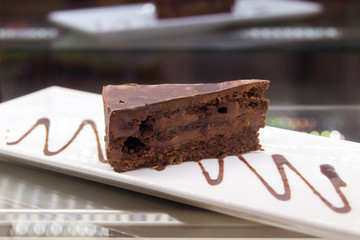 Wall Mural - Chocolate cake on plate on wood table . Pouring chocolate sauce on piece of chocolate cake cake truffle with black chocolate sauce