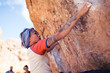 © Jeremy Francis - Petite asian woman rock climbing outdoors hangs from stone overhang with people watching