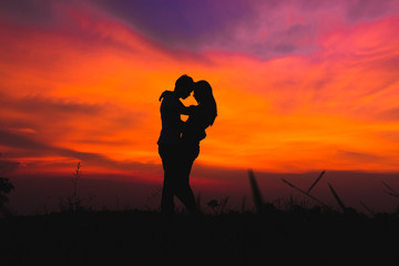 silhouette of romantic couple stand hugging on meadow at the sunset time . have a beauty blue sky.